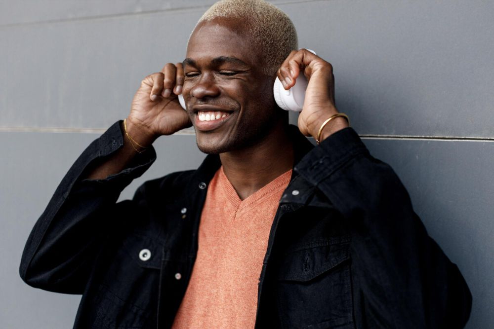 Man in a black jacket with an orange shirt wearing headphones and smiling