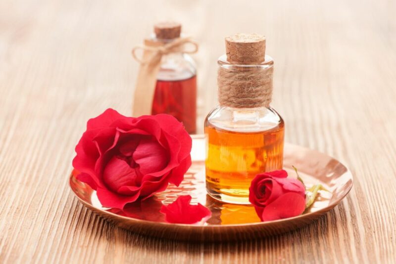 Rose buds on a plate with a glass bottle of rosewater and bottle of rose oil on a wooden table